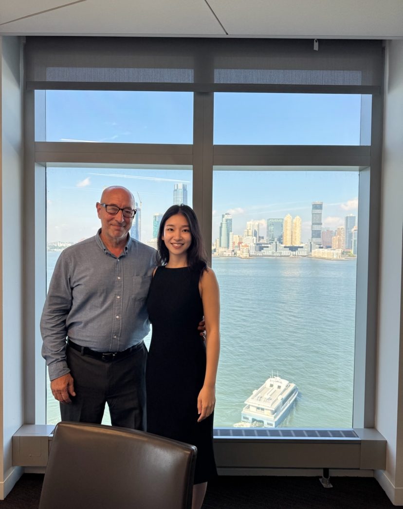 Cheng Shen with a guest in front of a window overlooking the Hudson River